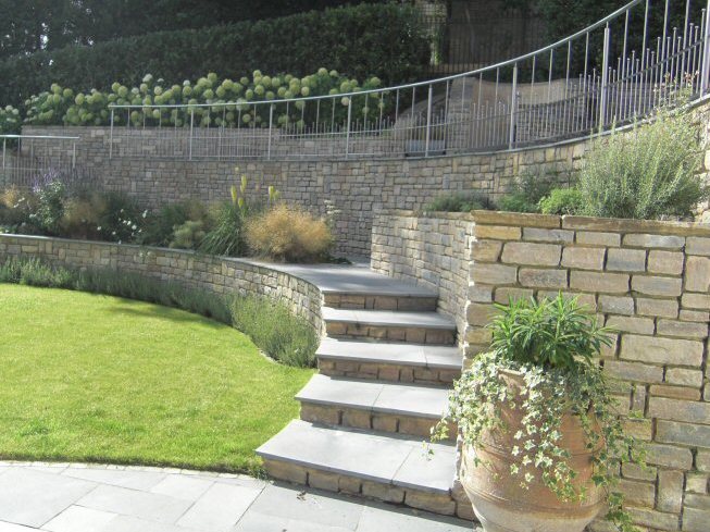 Large sloping garden design in Kenley, Surrey with stone faced retaining walls and stainless steel railings.