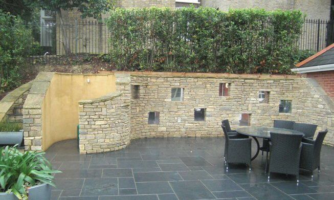 A sloping garden design in Kenley, Surrey, with stone walls, stainless steel rainings, and terraced levels. .