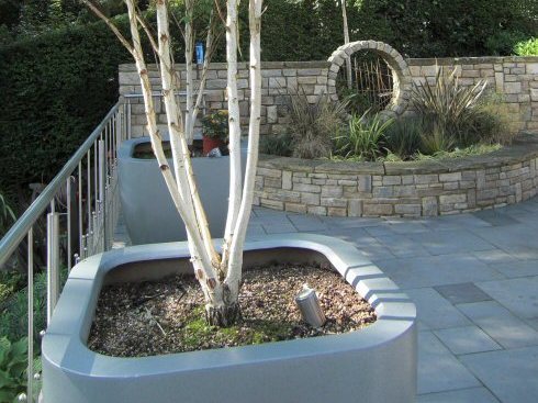 Large sloping garden design in Kenley, Surrey with stone faced retaining walls, moon gate and stainless steel railings.