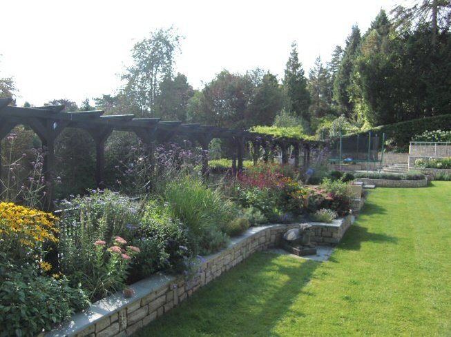 Large sloping garden design in Kenley, Surrey with stone faced retaining walls. black painted pergola, and stainless steel railings.