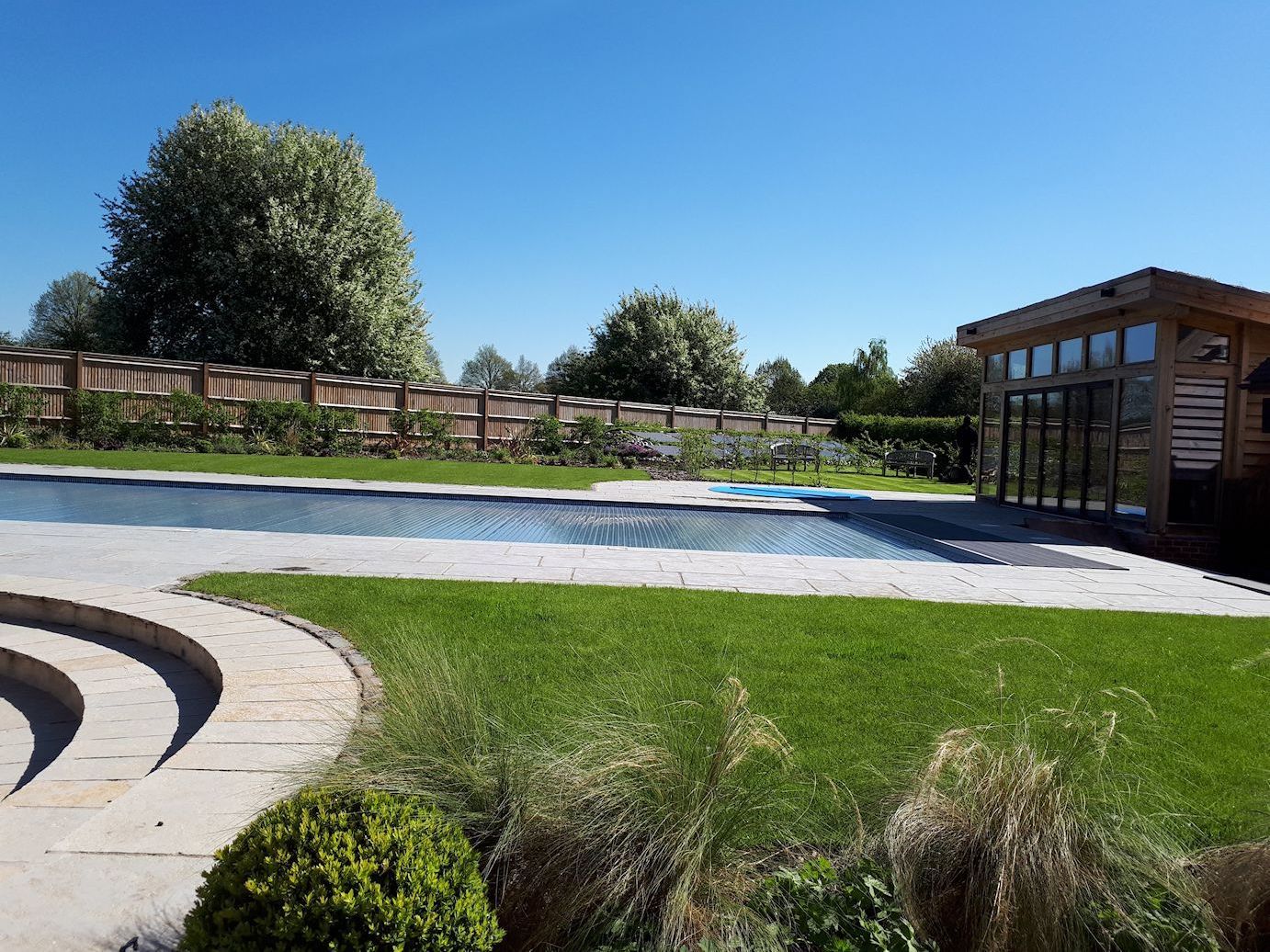 Garden design in Denham, Buckinghamshire with raised swimming pool terrace and curved steps.