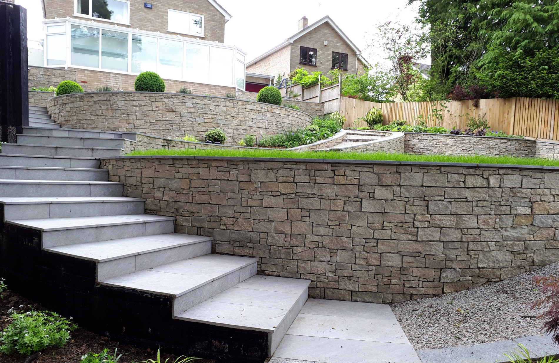 A sloping garden design in Sandhurst, Berkshire with stone faced retaining walls and terraced levels.